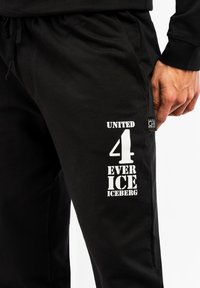 Sorte bomulds-sweatpants med et hvidt grafisk print med teksten "UNITED 4 EVER ICE" og et mærke med "ICEBERG." Elastisk talje med snørebånd.