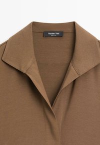 Braun, strukturiertes Polohemd mit klassischem Kragen und Etikettendetail. Der Stoff hat ein dezentes Rippmuster für zusätzlichen Reiz.