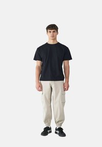 Czarna bawełniana koszulka zestawiona z beżowymi spodniami cargo z bocznymi kieszeniami, elastycznymi mankietami oraz czarnymi sneakersami z białymi akcentami.