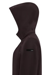 Giacca impermeabile marrone scuro con colletto alto e cappuccio integrato. Presenta una superficie liscia e una toppa nera con logo sulla spalla.