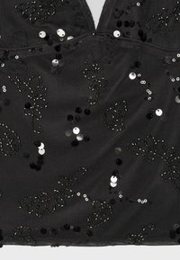 Tissu noir avec motifs floraux en sequins noirs et argentés et petites perles sur un fond en maille texturée.