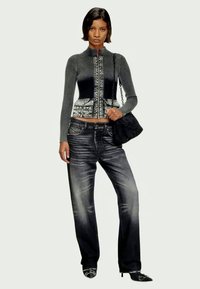 Γυναίκα που φοράει μια μαύρη και γκρίζα ζακέτα με φερμουάρ και ραβδώσεις, ξεθωριασμένα μαύρα τζιν, μαύρες μυτερές γόβες και κρατάει μια μαύρη τσάντα ώμου.