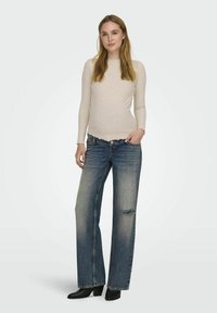 Lichtbeige geribbelde longsleeve top, gecombineerd met vervaagde blauwe wijde jeans met een versleten knie en raw hem. Zwarte enkelboots met hak.