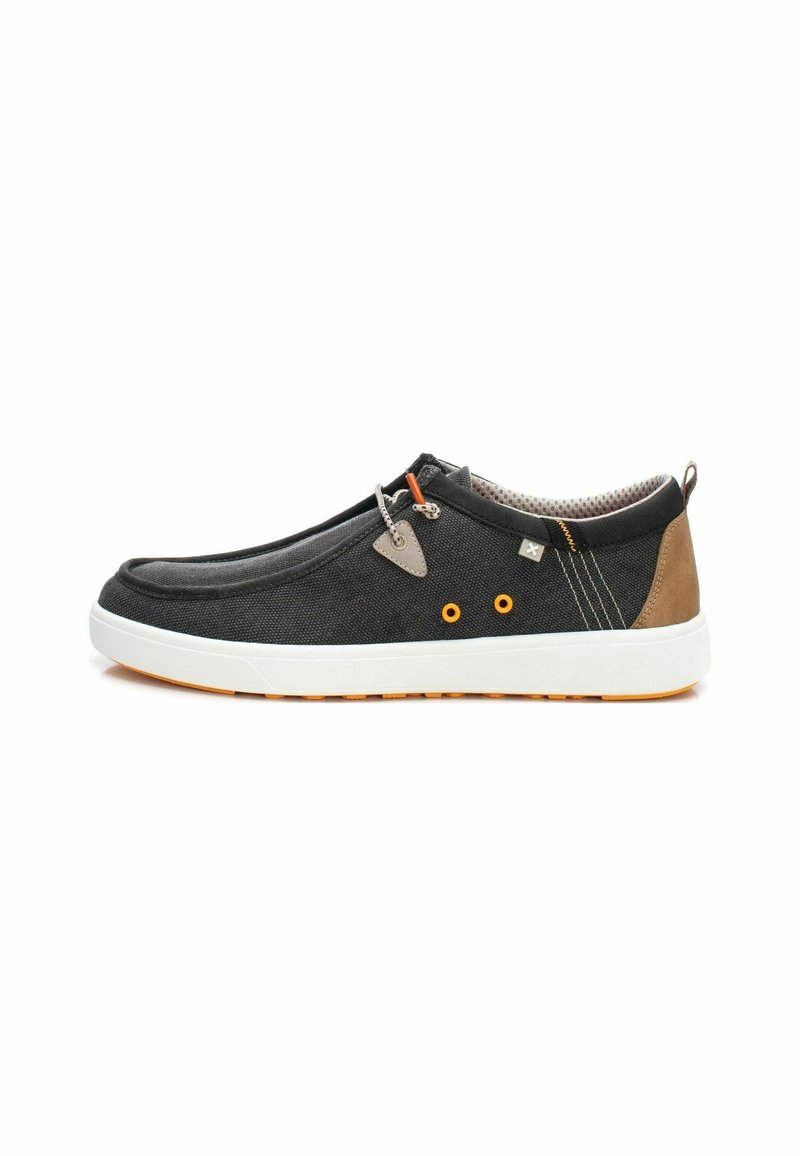 Zapatilla negra de lona con suela de goma blanca. Presenta detalles en naranja, talones marrones y tejido texturizado. Diseño sin cordones.