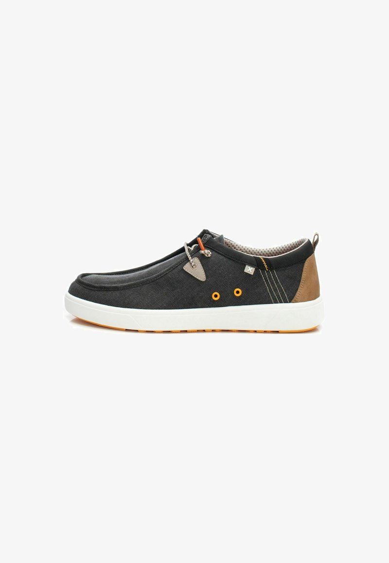 Zapatilla negra de lona con suela de goma blanca. Presenta detalles en naranja, talones marrones y tejido texturizado. Diseño sin cordones.