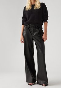 Czarne skórzane spodnie typu wide-leg z wysokim stanem, przednimi kieszeniami i wiązaniem w talii. Zestawione z czarnym swetrem prążkowanym.