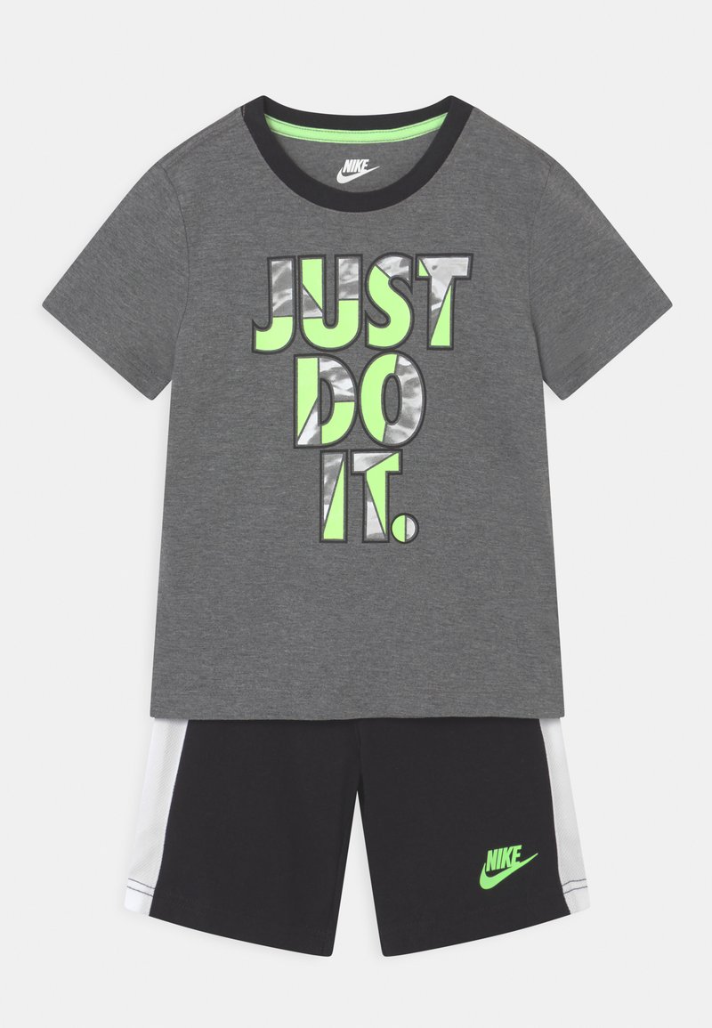 T-shirt grigio con la scritta "JUST DO IT" in lettere verdi e argento, abbinato a pantaloni corti neri con il logo Nike verde e accenti bianchi.
