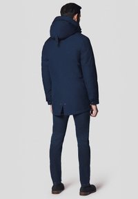 Granatowa parka z kapturem, z zapięciem na zamek i guziki, kieszeniami po bokach oraz delikatnym rozcięciem z tyłu. Odpowiednia na chłodne dni.