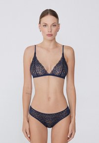 Námořnická krajková bralette s trojúhelníkovými košíčky a nastavitelnými ramínky, spárovaná s odpovídajícími krajkovými kalhotkami s vlnitými okraji a měkkou texturou látky.