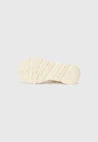 Cream-colored sneaker sole with textured rubber, featuring grooves and patterns for traction, curved edges, and no visible logos or branding.