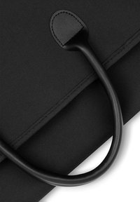 Czarna materiałowa torba o gładkiej fakturze, z zaokrąglonym czarnym skórzanym uchwytem oraz przeszywanym skórzanym akcentem u podstawy uchwytu.