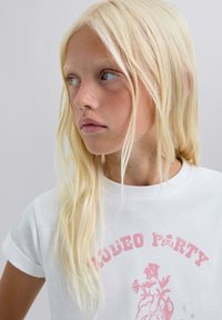 Witte t-shirt met korte mouwen, met een roze grafische print met de tekst "RODEO PARTY" en bloemontwerpelementen. Zacht katoenmateriaal.