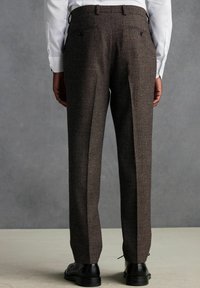 Braune maßgeschneiderte Hosen aus strukturiertem Stoff, mit geradem Bein, zwei hinteren Taschen und schwarzen Schuhen, die das Outfit vervollständigen.
