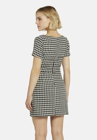 Schwarzes und weißes Hahnentrittmuster-Kleid mit kurzen Ärmeln, taillierter Taille und leicht ausgestelltem Rock. Glattes Material, runder Ausschnitt, Rückansicht.