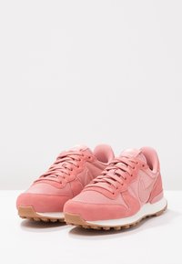 Růžové tenisky ze semišové a síťované látky, se šněrovacím designem, gumovou podrážkou a texturovaným vzorem na podrážce.