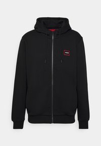 Sudadera negra con cremallera, hecha de tela suave, que presenta un parche de logo rojo en el lado izquierdo del pecho, capucha con cordón y puños y dobladillo acanalados.