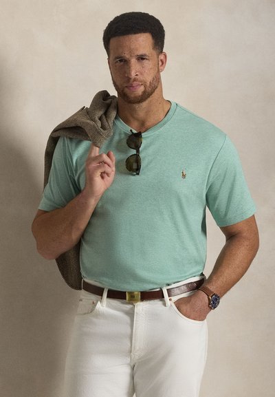 Μέντα πράσινο κοντομάνικο μπλουζάκι με μικρό λογότυπο. Συνδυάζεται με λευκό υφασμάτινο παντελόνι και καφέ ζώνη. Αξεσουάρ περιλαμβάνουν γυαλιά ηλίου και καφέ μπουφάν.