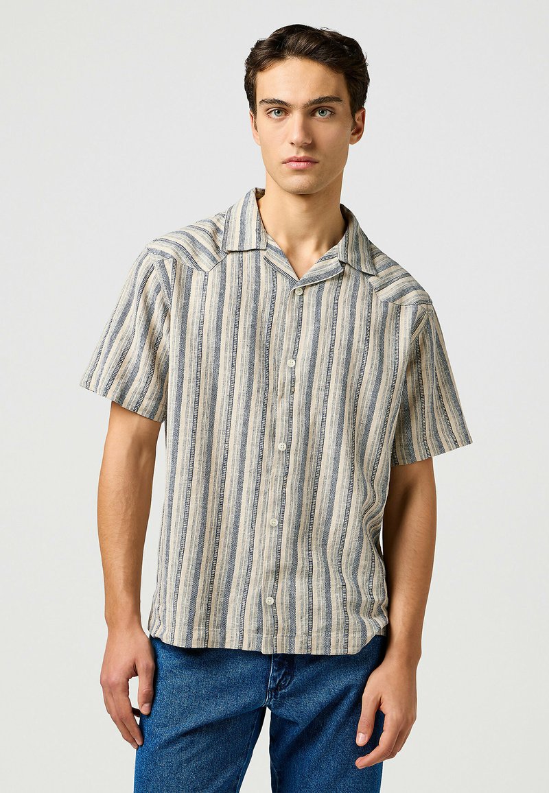 Korte mouwen, knoopshirt in lichtbeige met verticale blauwe en witte strepen. Heeft een puntige kraag en zachte, lichte stof.