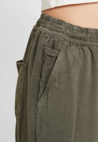 Olivgrön, avslappnade byxor med elastisk midja och sidofickor, tillverkade av lätt och texturerat tyg.