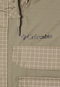 Olivgrön jacka med rutmönster, dragkedjefickor och Columbia-logotyp. Tillverkad av textil med strukturerad yta och justerbar dragsko i huvan.