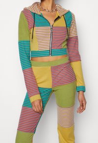 Ensemble assorti multicolore comprenant un sweat à capuche court zippé et un pantalon taille haute. Motifs rayés en vert, jaune, rose et bleu.
