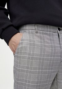 Szare i czarne spodenki w kratkę o gładkim materiale, z bocznymi kieszeniami i zapięciem na guzik. Model nosi czarną bluzę.