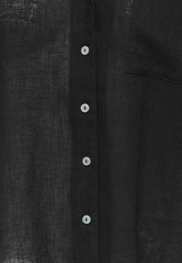 Sort linnedragt med hvide knapper i midten og en synlig brystlomme på højre side.