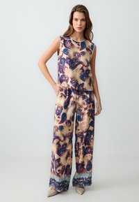 Twee-delige outfit bestaande uit een mouwloos topje en broek met wijde pijpen. De stof heeft een bloemen paisley patroon in blauwe, crèmekleurige en mauve tinten.