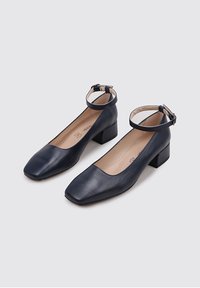 Zapatos de cuero azul marino de punta cuadrada con tacón bajo y correa en el tobillo. Textura lisa, diseño minimalista y sin patrones visibles.