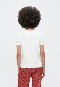 Hvid kortærmet T-shirt med en standard rund hals, kombineret med røde mønstrede bukser med geometriske former. Struktureret stof er synligt.