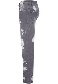 Vaqueros ajustados de denim gris con un patrón de salpicaduras blancas y detalles desgastados. Presentan una cinturilla estándar y cinco bolsillos.