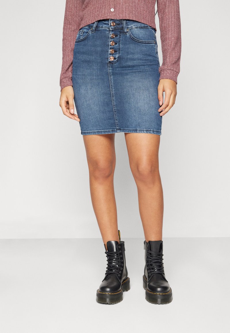 Denim mini skirt in blue with a pencil shape, five-button front, two pockets, and stitched detailing. Paired with black lace-up boots.
