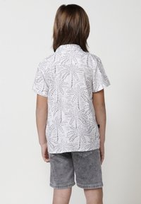 Balta trumpų rankovių marškiniai su pilkų delno lapų raštu, derinami su pilkais džinsiniais šortais. Medžiaga lengva, tinkama šiltam orui.