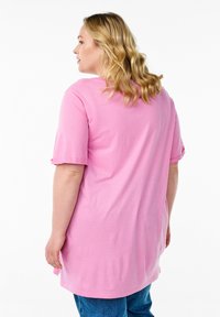 Pink cotton t-shirt with short sleeves and a relaxed fit, featuring a slightly longer back hem and visible stitching details.
