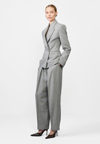 Szary dopasowany żakiet z wyraźnymi klapami i pojedynczym zapięciem, w połączeniu z spodniami o wysokim stanie i szerokimi nogawkami. Lśniące czółenka o spiczastym nosku.