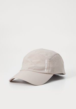 Lys beige cap laget av glatt stoff, med en buet skjerm, perforert detaljering på sidene, og en hvit "SALOMON" logo.