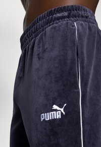 Σκούρες μπλε βελουτέ παντελόνες φόρμας με υφή, ελαστική μέση και λευκό λογότυπο PUMA στο αριστερό μηρό. Διαθέτουν πλαϊνές σχισμές.