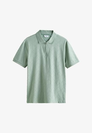 Hellgrünes Poloshirt mit kurzen Ärmeln, strukturiertem Wellenmuster und vorderem Reißverschluss unter dem Kragen.