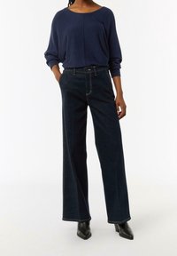 Navy wijde jeans met contraststiksel, met een hoge taille en een taillering. Gecombineerd met een losvallend navy top en hoge laarzen.