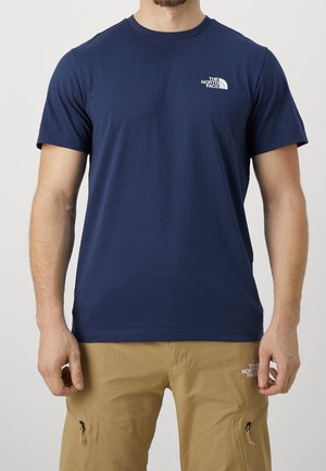 Homme portant un t-shirt bleu marine à manches courtes et un pantalon cargo beige, tous deux avec le logo The North Face.
