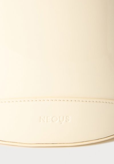 Gros plan d'une surface en cuir couleur crème avec une couture soignée et le nom de la marque embossé « NEOUS » centré sous la couture.
