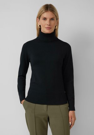 Schwarzer Rollkragenpullover aus gerippter Textur mit langen Ärmeln und einer figurschmeichelnden Passform. Kombiniert mit olivgrünen, taillierten Hosen.