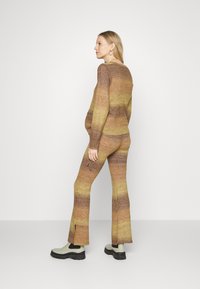 Suéter em degradê castanho e amarelo e calças largas com fendas laterais, combinados com botas de tornozelo verdes. Textura suave, ajuste descontraído.