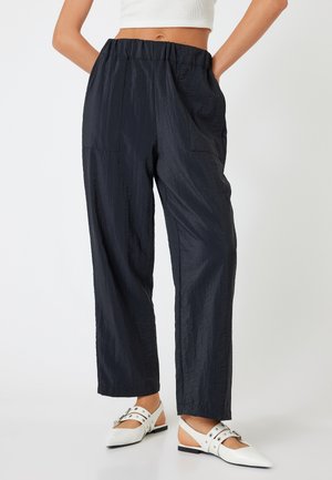 Pantalons bleu marine amples en tissu froissé, dotés d'une taille élastique et de poches latérales, accompagnés de chaussures blanches à bout pointu.