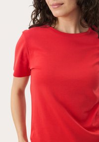 T-shirt rouge à manches courtes avec col rond, fabriqué à partir d'un tissu lisse, offrant une coupe décontractée et un design simple, mettant en avant la couleur et la texture.
