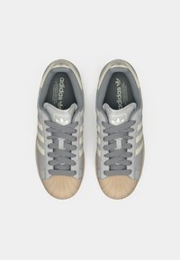 Sneakers grigie in materiale liscio, dettagli beige, punta rotonda, design con tre strisce e lacci piatti grigi. Marchio classico Adidas.