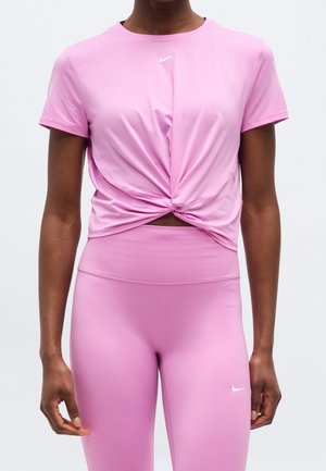 Vrouw draagt een roze korte mouwen geknoopte crop top en leggings met een hoge taille met kleine witte Nike-logo's op de borst en dij.