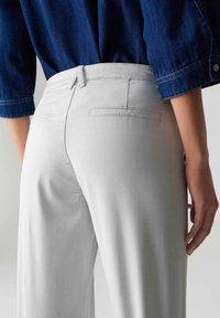 Pantalons larges gris clair avec poches arrière, taille cintrée et tissu doux. Associés à une chemise en denim bleu foncé, mettant en avant un style décontracté.