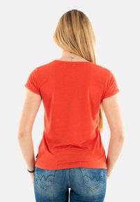 T-shirt rouge à manches courtes avec un col rond, fabriqué en tissu doux. Coutures visibles et manches enroulées. Assorti à un jean bleu.