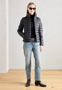Doudoune noire avec un col haut, légère, au design matelassé, associée à un jean bleu clair et des bottines noires. Accents matériels minimalistes.